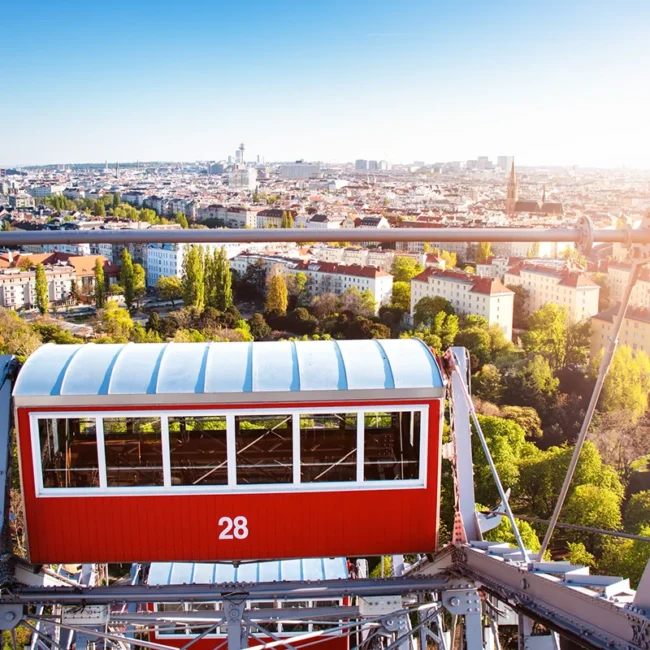 Ein roter Waggon des geschichtsträchtigen Wiener Riesenrads im Wiener Prater, von dem aus sich ein weiter Panoramablick über die sonnige Stadt Wien eröffnet.