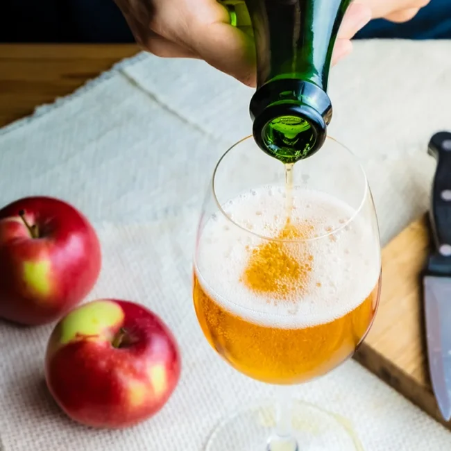Goldener Apfelmost wird im Waldviertel aus einer dunklen Flasche in ein Weinglas eingeschenkt, während daneben zwei frische Äpfel liegen.