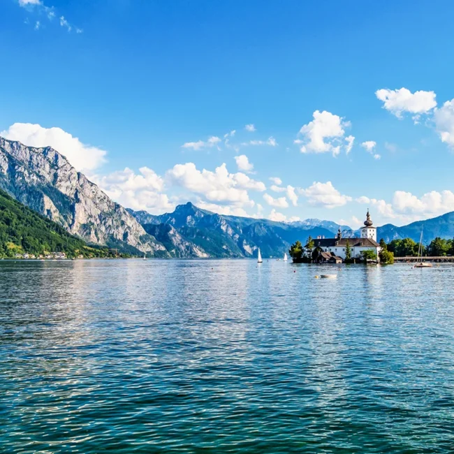 Das malerische Seeschloss Ort auf einer kleinen Insel im tiefblauen Traunsee, eingerahmt von der imposanten Bergkulisse des Salzkammerguts in Österreich.
